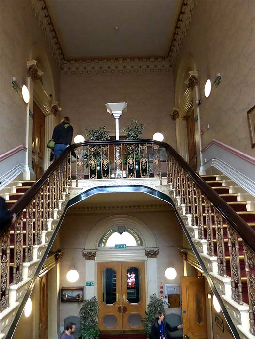 The sweeping staircase of the Oldham Lyceum and the stained glass window illuminating it.